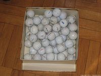 Top view of box containing roughly 70 white golf balls