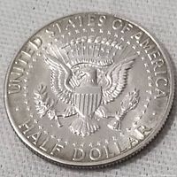 Reverse side of 1964 USA Kennedy Half Dollar featuring the heraldic eagle with shield, olive branch, arrows, surrounded by stars and inscriptions 'UNITED STATES OF AMERICA' and 'HALF DOLLAR'.