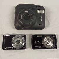 Top view of 3 digital cameras including Fujifilm Instax Mini 11, Sony Cyber-shot, Kodak Easyshare Touch