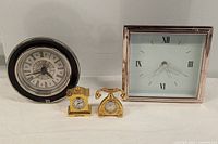 Four desk clocks arranged on white surface showing their faces and frames