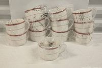 Full set of stacked Ultra Bone China cups and saucers wrapped mostly in plastic, showing the red and black lined rim pattern on white china.