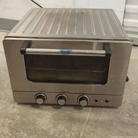 Front view of stainless steel Cuisinart Brick Oven showing handle, glass door, and three control knobs.