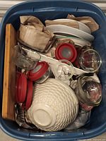 Photo showing a container filled with assorted dishware including glass bowls, ceramic plates, and items wrapped in brown paper for protection.