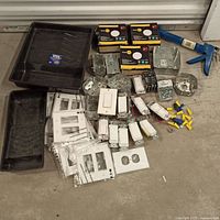 Photo of assorted electrical switches, faceplates, metal and plastic switch boxes, screws, wire connectors, and other related hardware items arranged on floor.