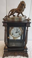 Full front view of the lion mantel clock showing the brass lion atop the granite base, dark wood case with glass front, and clock face.