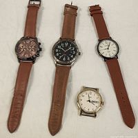 Four men's wristwatches arranged in a row on a flat surface, varying in dial and strap style.