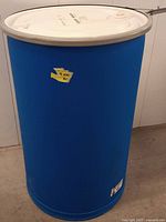 Blue plastic shipping barrel showing full side view with white lid on top, minor surface wear.
