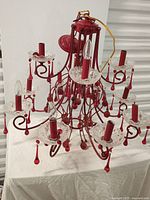 Full view of red metal chandelier with multiple arms and red glass droplet decorations on a white surface.