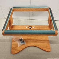 Front angled view of rug hooking frame on wooden stand with hardware screws included in plastic bag.