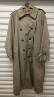 Front view of beige double-breasted trench coat on hanger against storage unit door