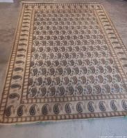 Overall front view of vintage Kashan rug largely beige with brown and muted colored paisley motifs laid on floor.
