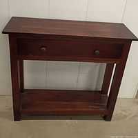 Front view of a wood console table showing the drawer and lower shelf.