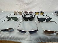 Top-down view of 10 pairs sunglasses on grey surface showing variety of frame styles and lens colors.