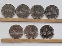 Reverse sides of 7 Canadian Voyageur dollar coins with the canoe and two voyageurs design, dated 1968, 1969, 1981, 1983, 1985, and 1986.