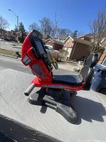Side profile photo showing red motorcycle-style arcade racing toy with seat and black base.