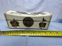 Side view of the porcelain jewelry box shaped like a curved pillow with floral patterns and metal latch, measuring approximately 12 inches long.