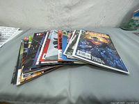 Stack of various comic books laid flat, shows multiple issues in typical comic book sizes and colorful covers.