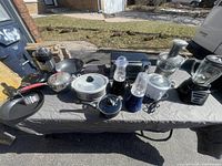 Wide shot of assorted cookware and small kitchen appliances on table outdoors