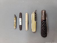 Five vintage pocket knives laid flat with handles visible, showing variety in size and materials.
