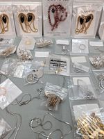 Close-up of costume jewelry including gold-tone earrings with black stones, pink beaded necklace, and various silver-tone pieces presented in plastic bags.