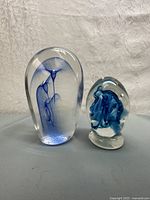 Front view of pair of glass paperweights with blue internal designs on textured fabric background