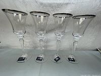 Four clear wine glasses with platinum silver trim at the rim, standing upright with branded stickers on the bases.
