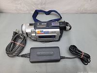 Sony digital Handycam DCR-TRV17 camcorder alongside power charger with cables and a blue strap attached to the camera.