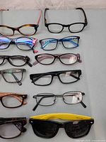 Top view of 10 eyeglass frames in different styles and colors including tortoiseshell, black, and one pair with yellow temples showing sunglasses.