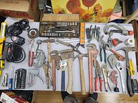 Top-down photo of assorted hand tools laid out on table including hammers, wrenches, pliers, and tape measures