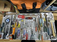 Top-down view of all tools laid out on table with tool bag in background showing variety and condition.