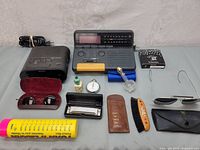 Full lot photo showing all items including two vintage radios, sunglasses, harmonica, stopwatch, perfume bottle, brush, comb, mint tin, and hairpin.