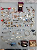 Overview of entire lot displaying a diverse collection of vintage costume jewelry arranged on a gray surface