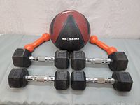 Photo showing four black hex dumbbells, two small orange hand weights, and a Nike workout ball marked 8 lb (3.63 kg)
