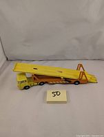 Side view of the full length car transporter truck displaying the yellow cab and orange trailer with tilted upper deck.