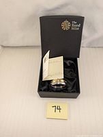 The black presentation box with the silver-plated bell inside and certificate of authenticity partially visible.