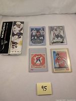 Four hockey cards displayed on a white surface with a post-it note labeled '95'. Cards include a Tim Hortons NHL Star Sticks collectible and three different hockey cards featuring Alex Ovechkin, all in protective sleeves or boxes.