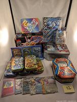 Overview photo showing multiple Pokemon card tins, jumbo Blastoise EX card, assorted cards displayed in front, and card stand from Terapagos UPC
