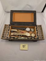 Open wooden decorative box containing watches, ring, watch faces, money clip, key chain, and medical alert bracelet arranged inside