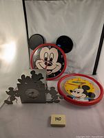 Lot showing all three clocks: two round Lorus Mickey Mouse wall clocks with red edges and black ears, and one silver and black Schmid Michael Graves desk clock with Mickey Mouse silhouette design.