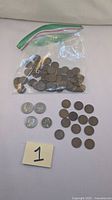 Photo of a plastic bag containing multiple coins including quarters, nickels, and various pennies spread out for display, labeled with number 1.