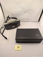 Vintage Kodak Tourist II camera in silver and black with strap displayed beside a number 121 label on a white backdrop.