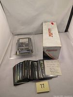 Photo showing a box with Magic The Gathering logo alongside a stack of sleeved trading cards spread out with some card sleeves and a label describing card counts and set types