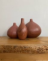 Front view of three ceramic vases with wood grain finish on wooden shelf.
