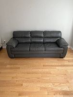 Front view of the three-seat leather sofa showing padded back cushions, armrests, and base with minor wear.