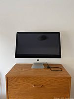 Front view of the Apple iMac desktop showing screen and stand on wooden cabinet.