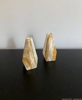Front angle view of two vintage onyx candle holders placed on a black surface against plain wall.