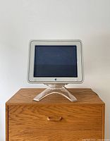 Front view of the vintage Apple Studio Monitor showing the white bezel and black Apple logo beneath the screen, mounted on clear acrylic stand.