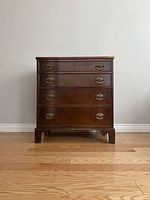 Front view of the vintage wooden dresser with four drawers, brass drop handles, and wood finish.