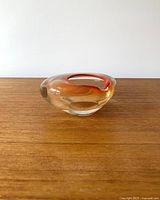 Side view of the vintage glass ashtray on a wooden surface showing thick clear glass and red swirl detail.