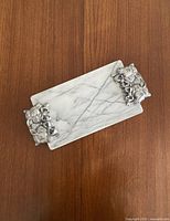 Top view of the rectangular white marble tray showing natural veining and silver-tone sculptural metal handles at each end.